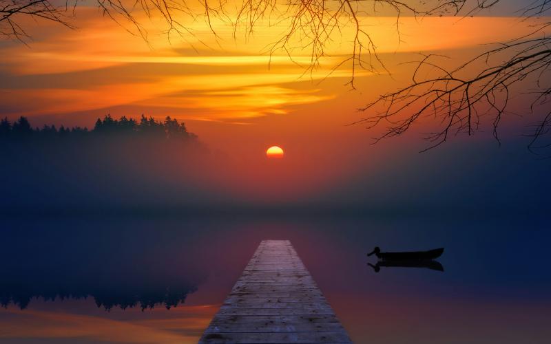 Sunset over a tranquil lake, with a dock and small boat silhouetted against the vibrant sky.
